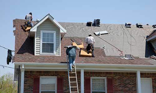 Three workers on a roof installing new shingles